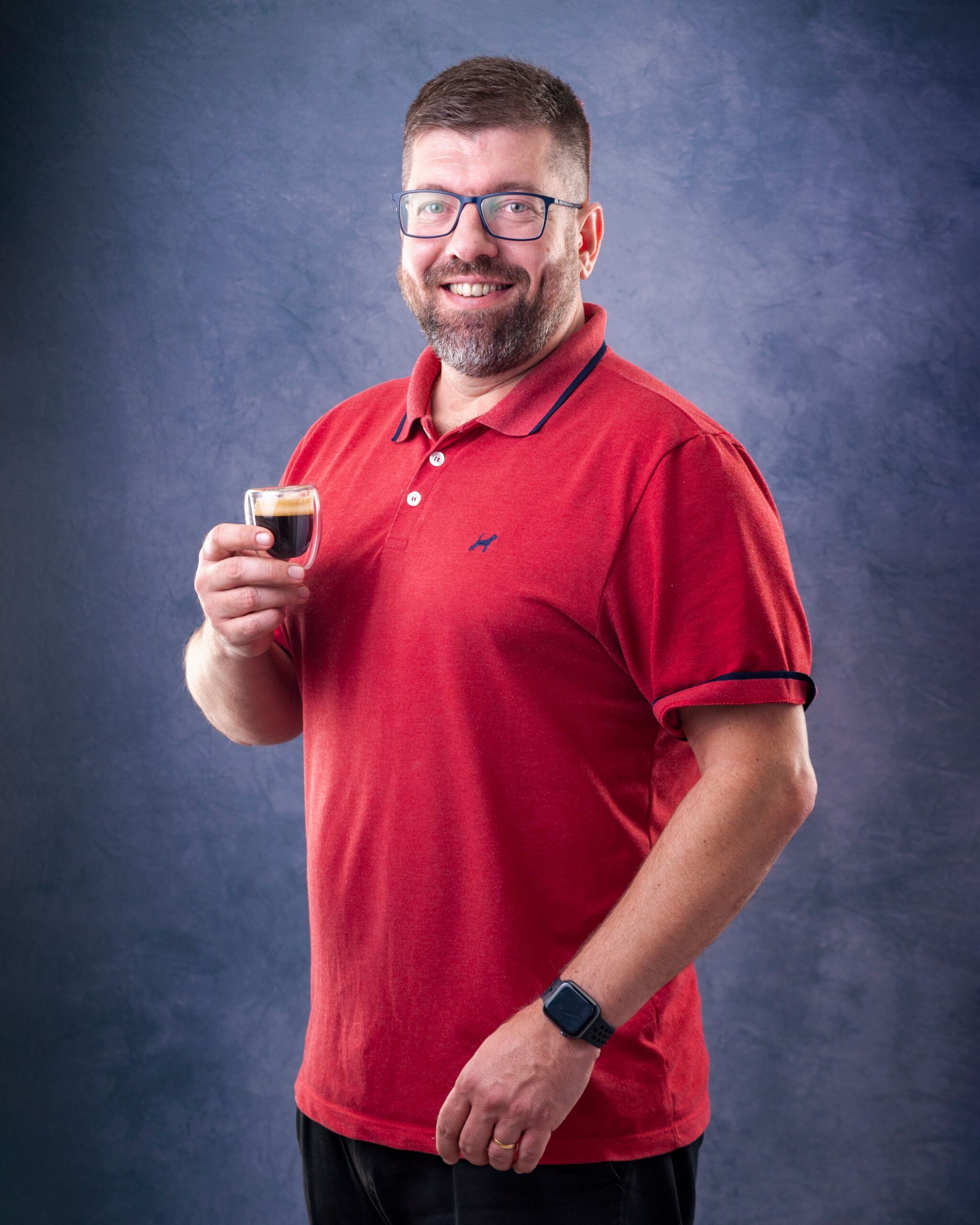 Portrait of a smiling man in glasses holding an espresso cup indoors.