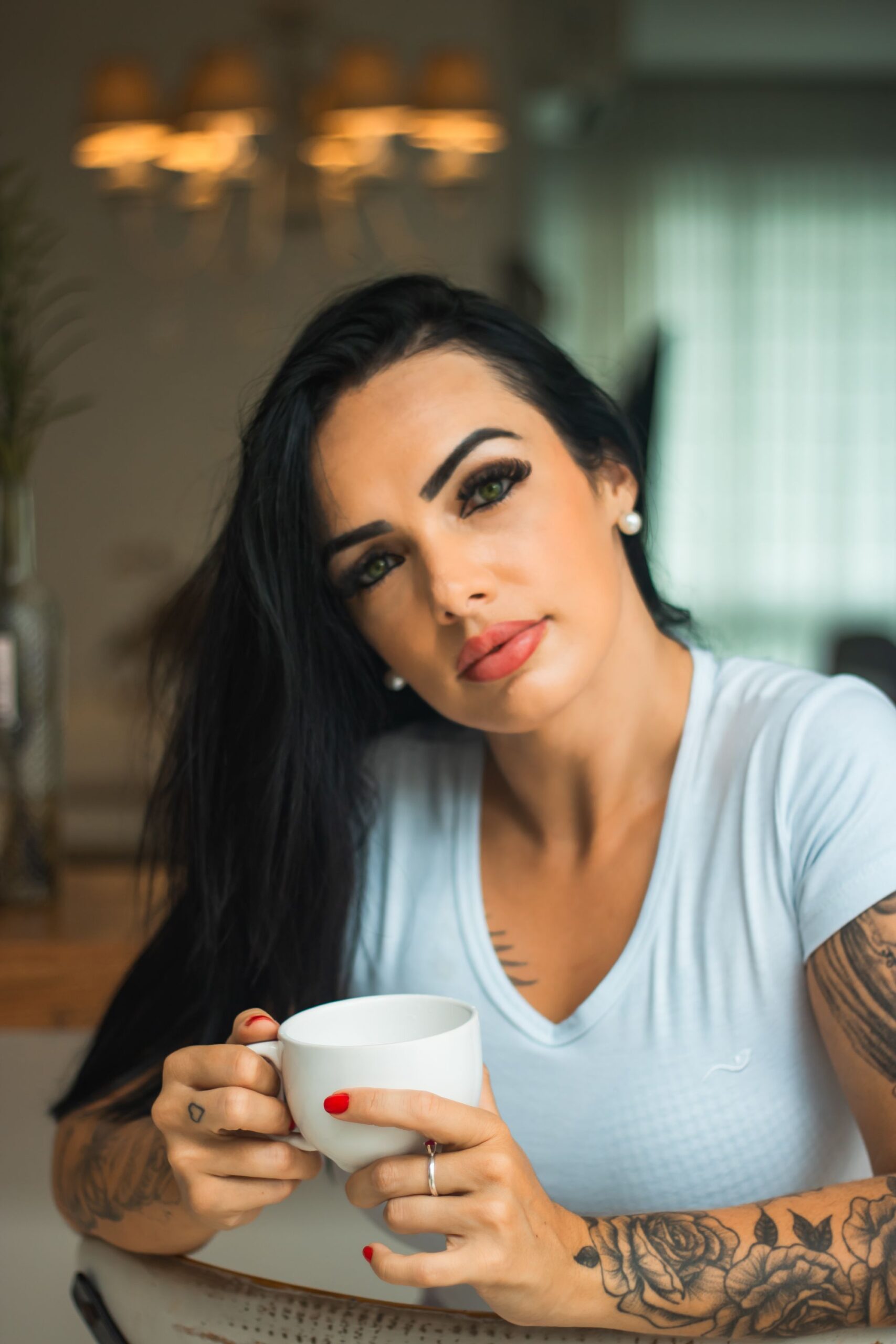 Portrait of a woman with tattoos holding a coffee cup indoors, showcasing a relaxed lifestyle.